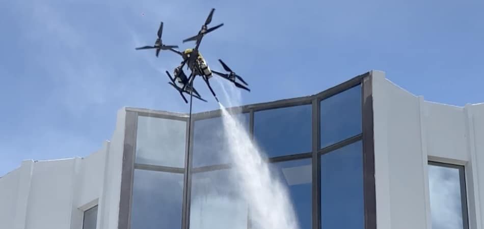 Dron pulverizando agua tratada sobre las ventanas de un muro cortina curvo